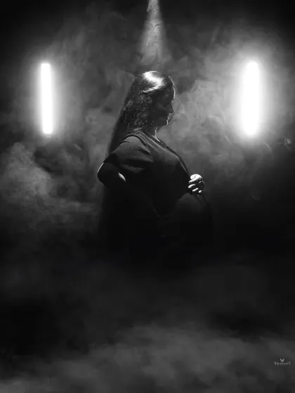 A dramatic profile silhouette enhanced by smoke and two vertical lights. This artistic black and white shot emphasizes the beautiful curve of the baby bump.