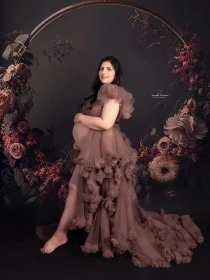 A dark and moody studio portrait. This client is wearing a brown ruffled maternity gown, seated in a floral hoop prop that creates a stunning, artistic frame around her.