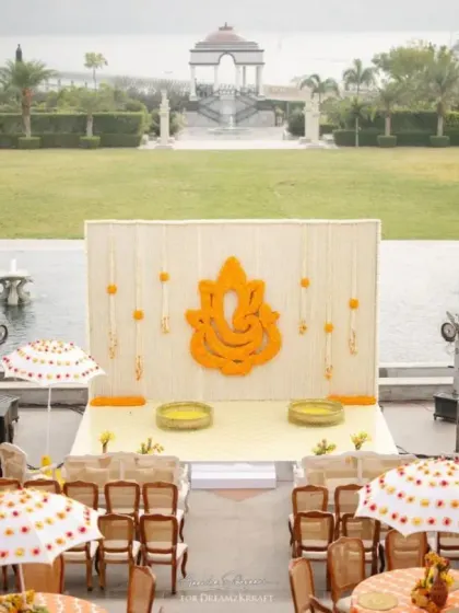The main stage for the Haldi ceremony, featuring a Ganesha motif made of marigolds, set against the stunning backdrop of the infinity pool and lake at Raffles, Udaipur.