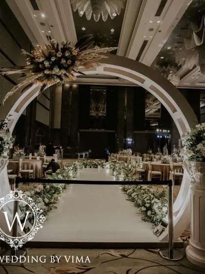A classic and elegant reception setup symbolizing everlasting love. The stage features a modern, minimalist backdrop with custom monograms, floral arrangements, and soft lighting.