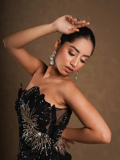 A graceful, artistic pose that shows off the intricate sequin work on the strapless top. The focus is on the texture and craftsmanship of the garment.