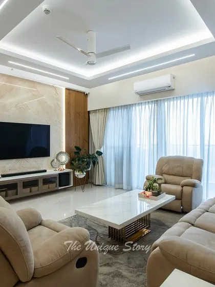 A comfortable and inviting view of the living room, centered around the plush recliners. The layered lighting from the false ceiling and the natural light from the large windows create a bright and airy atmosphere perfect for relaxation.