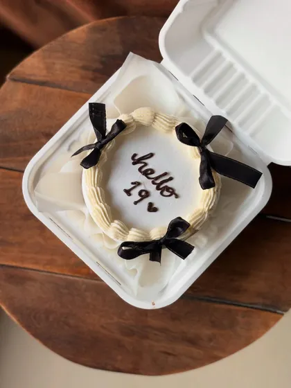 A chic, Pinterest-inspired bento cake for a 19th birthday. The design is simple and elegant, with "hello 19" written on a white cake adorned with four black satin bows.