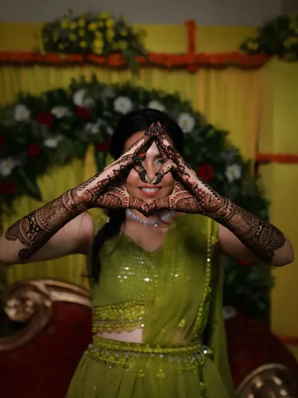 A playful shot from a mehndi ceremony, with the bride making a triangle with her hands to show off the full design.