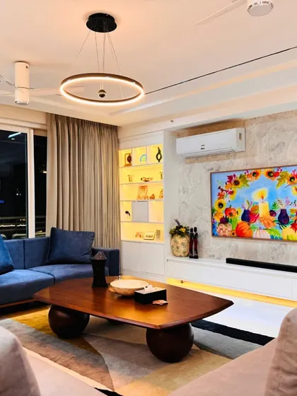 A comfortable and stylish living room with a mix of blue and beige sofas, a large wooden coffee table, and a feature wall with textured panels and backlit shelving.
