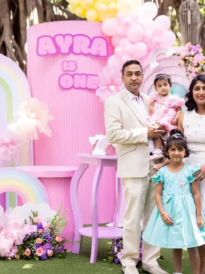 The full family posing in front of the vibrant, pastel-pink backdrop at Ayra's party.