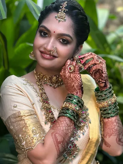A candid shot of the bride adjusting her earring. This image highlights the detailed henna work and the beautiful harmony between the makeup, green bangles, and antique-finish temple jewellery.
