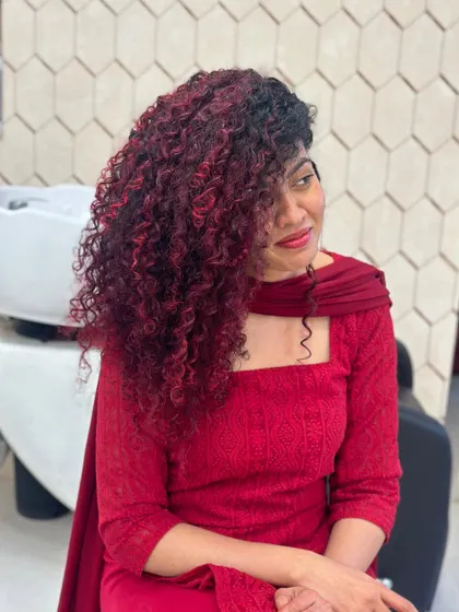 A full view of this stunning red balayage on long, beautiful curls. The color is strategically placed to create dimension and movement, making the curls pop. This shows how vibrant color can work in harmony with natural texture.