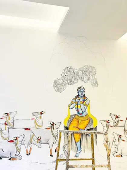 The Krishna and cows mural in progress. Here, the central figure of Krishna is colored in, seated on a ladder as I work on the intricate details of the surrounding trees and cows.