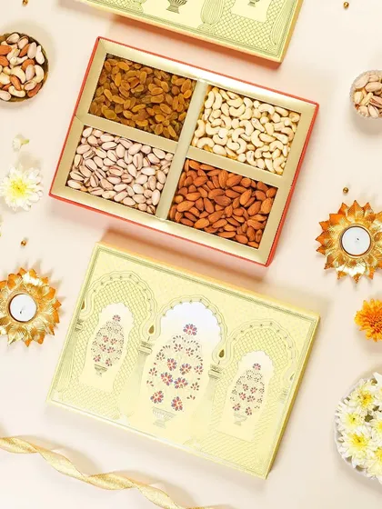 A festive flatlay of a yellow dry fruit gift box with traditional Indian arch designs. The arrangement with flowers and diyas creates a warm and inviting look for a Diwali catalog.