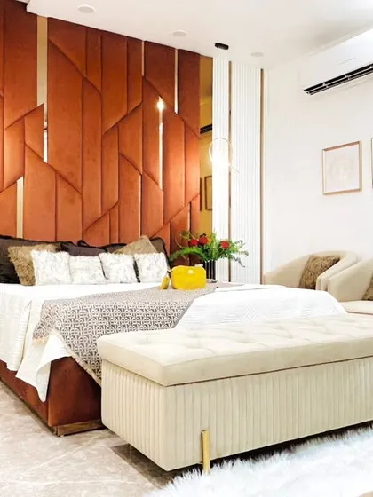 A modern bedroom retreat featuring a striking geometric upholstered headboard in a rich rust color. The space is designed with layered textures and warm, earthy tones for a cozy yet sophisticated feel.