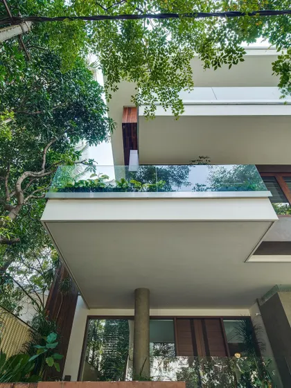 A detail of a cantilevered balcony at Kanasu, where a glass railing provides an unobstructed view of the trees, making the greenery an integral part of the home's facade.