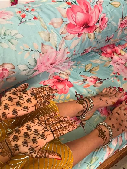 A minimal bride's complete look, with lotus buti patterns on her hands and simple, elegant designs on her feet, adorned with silver anklets.