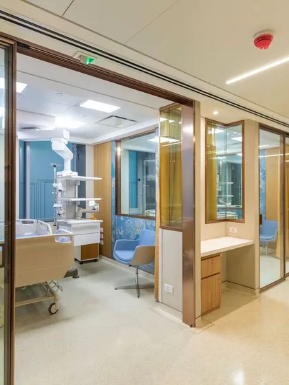 This ICU area at Breach Candy Hospital uses glass partitions to maintain visibility while providing privacy. The design incorporates calming blue accent walls and wood tones, demonstrating that even high-tech areas can be designed with empathy.