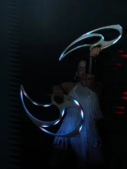 A posed shot in a fringed dress with my LED fans. The contrast between the dark background and the glowing props creates a dramatic effect.