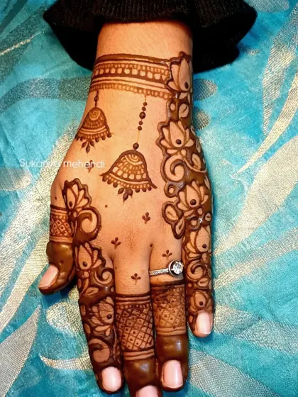 A delicate and stylish design perfect for Karvachauth. This Arabic-style mehendi features hanging jhumkas and lotus vines on the back of the hand.