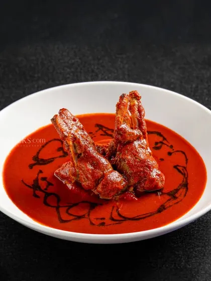 Tandoori prawns served in a rich red gravy, presented in a minimalist white bowl.