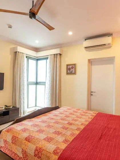 Another view of the guest bedroom, showing the simple TV unit and the corner window that provides natural light.