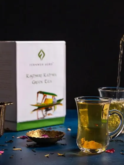 A wider shot of the Kashmiri Kahwa pour, showing the product box and ingredients. This provides context and is great for a complete brand narrative.