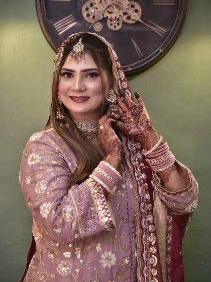 The bride is adjusting her earring, a classic bridal pose. This highlights her intricate henna and the soft curls in her hair.