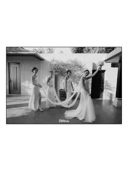 A playful, black and white shot of the bride and her bridesmaids, with the long train of her dress connecting them.