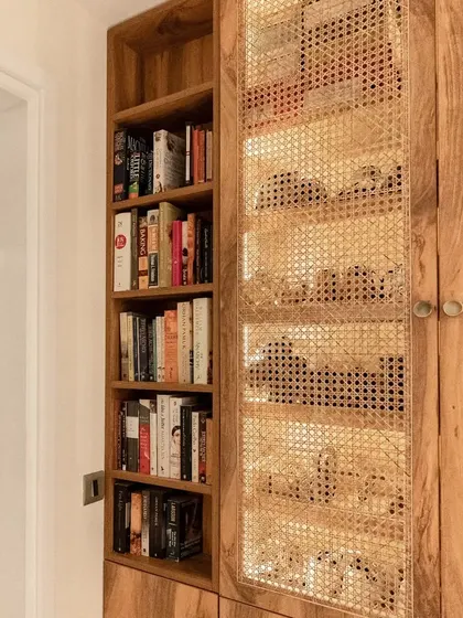 A close-up of the rattan and wood cabinet, designed to house books and other collections. The natural texture of the rattan adds a layer of warmth and craft to the space.