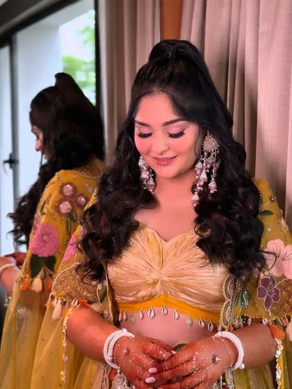 A fun and flirty high half-ponytail with bouncy curls. This is a great hairstyle for a Mehendi or Haldi ceremony, keeping the hair off the face while still showing off its length.
