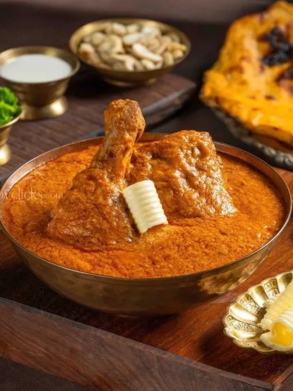 A homestyle Butter Chicken, rich and creamy, served in a brass bowl with a dollop of butter on top.