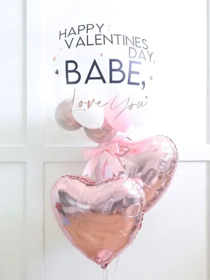 A sweet and modern Valentine's balloon bunch. It features a large bubble balloon with a custom message, paired with two rose gold heart foil balloons.