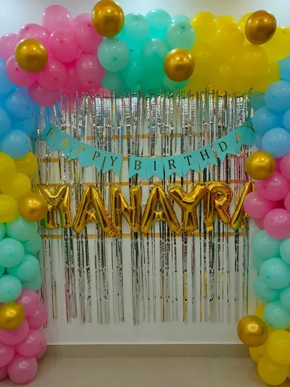 A simple and colorful balloon arch with a silver shimmer curtain and a 'Happy Birthday' banner, perfect for a vibrant home party.