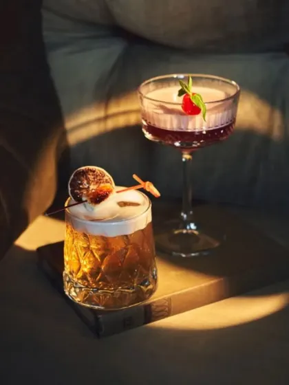 A pair of expertly crafted cocktails, catching the light. Our bartenders use premium spirits and fresh ingredients to create drinks that are as beautiful as they are delicious.