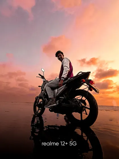 A portrait of a man on his bike at the beach during a stunning pink and orange sunset. The reflection on the sand creates a mirror image, adding to the beauty of the shot.