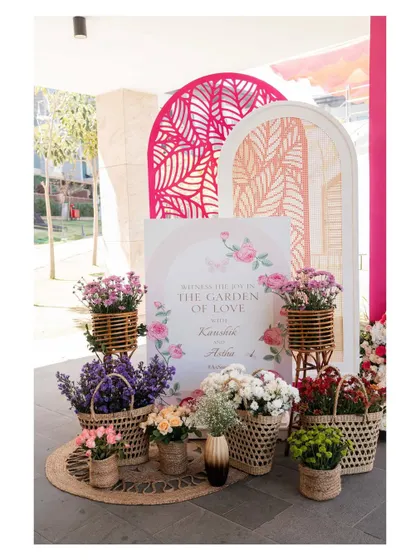 A welcome sign for a Mehendi ceremony, surrounded by baskets of fresh flowers. The "Garden of Love" theme is introduced right at the entrance, setting a romantic and floral tone for the event.