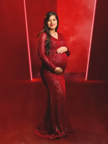 A bold and confident portrait of a mom-to-be in a sparkling red sequin gown against a dramatic red backdrop with neon lights.