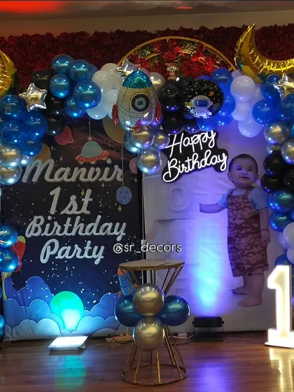 Our custom 'Space' theme party decor includes a personalized backdrop with the birthday boy's name, a balloon arch with planet and rocket foils, and a photo display area.
