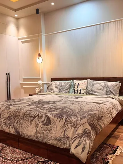 A classic and elegant bedroom with dark wood furniture, a botanical print duvet, and traditional wall molding. The pendant lights on either side of the bed add a modern touch.