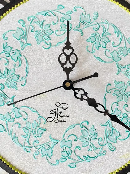 A close-up of the center of a 20-inch wall clock, showing the delicate teal stencil work on a clean white background.