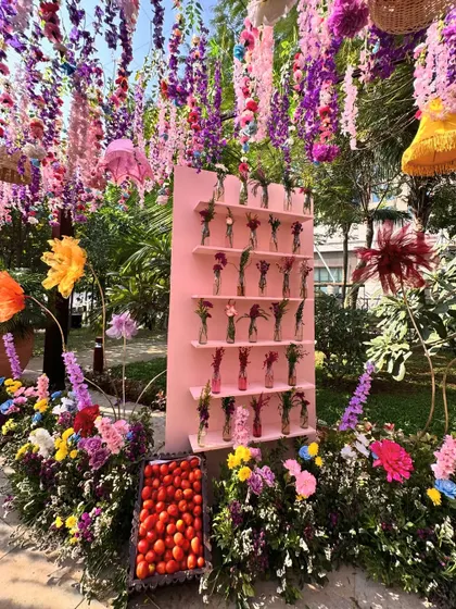 A vibrant display of flowers in individual vases on a pink shelf, creating a wall of color and fragrance. Fresh strawberries add a playful, edible element.