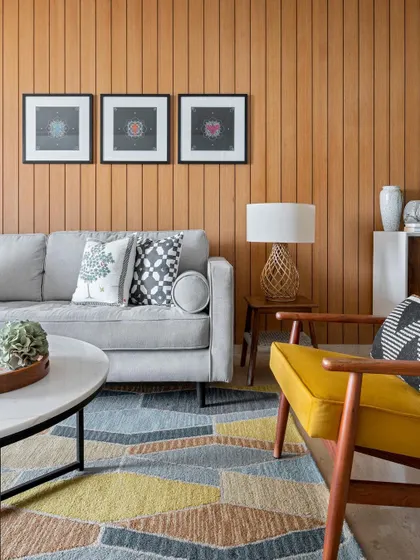 A mid-century modern living room with a full wall of vertical wood paneling. The bright yellow armchair and geometric rug add a playful pop of color and pattern.