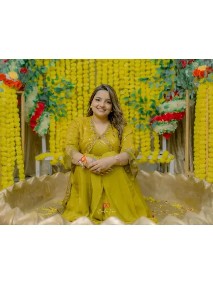 A classic portrait of the bride at her Haldi ceremony, seated in a traditional urli bowl against a vibrant marigold backdrop.