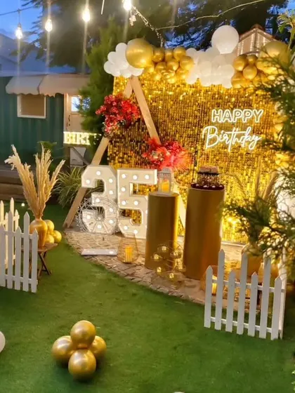 A stunning 35th birthday setup in a garden. The gold sequin backdrop is framed by a teepee structure, with marquee numbers and warm string lights creating a magical glow.
