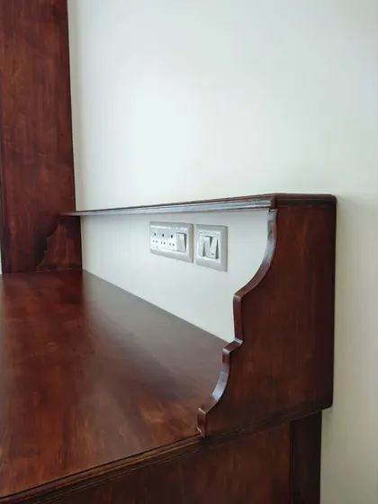 A detail shot of the work desk, showing the elegant curved design of the back panel and the integrated power sockets for convenience.