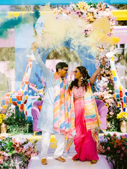 A blast of color! Laxmi and Roshan are framed by yellow and blue smoke, creating a dynamic and unforgettable image from their Haldi celebration.