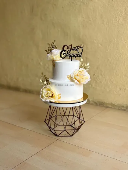 A classic two-tier "Just Engaged" cake, elegantly decorated with white roses and gold leaf accents. We teach techniques for applying gold leaf for that touch of luxury.