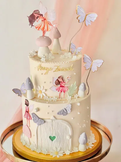 An enchanted fairy garden cake. This two-tiered design features a fairy door, fondant mushrooms, and delicate printed fairies and butterflies.