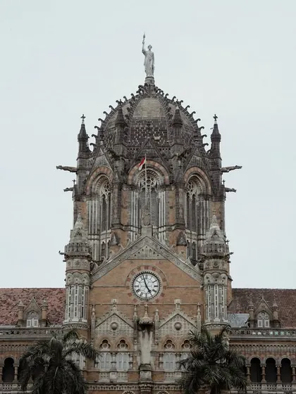 Wide shots of the CSMT building, showcasing its intricate Victorian Gothic design. The presence of the iconic red double-decker buses adds to the vintage charm.