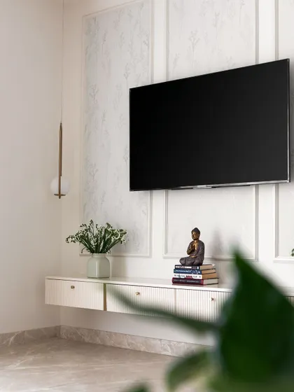 This minimalist floating TV unit in white features grooved drawers and is set against a wall with a subtle floral wallpaper and classic beading.