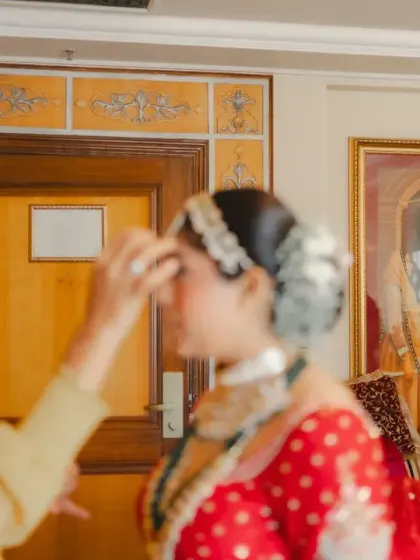 A soft-focus shot of the mother of the bride applying a bindi, a tender and emotional getting-ready moment. The painting in the background adds a layer of artistic, traditional context.