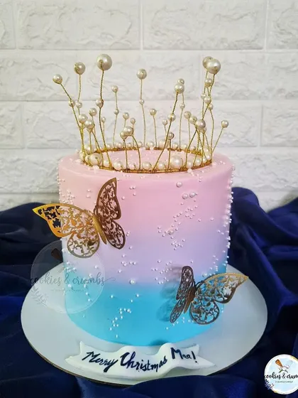 A beautiful Christmas cake with a pink and blue ombre effect. The design is elevated with a delicate pearl crown and golden butterflies, making it feel magical.