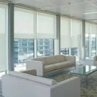 Simple, off-white roller blinds installed across a wall of windows in a bright, open office or living space. They provide a clean, uniform look and effective sun protection.